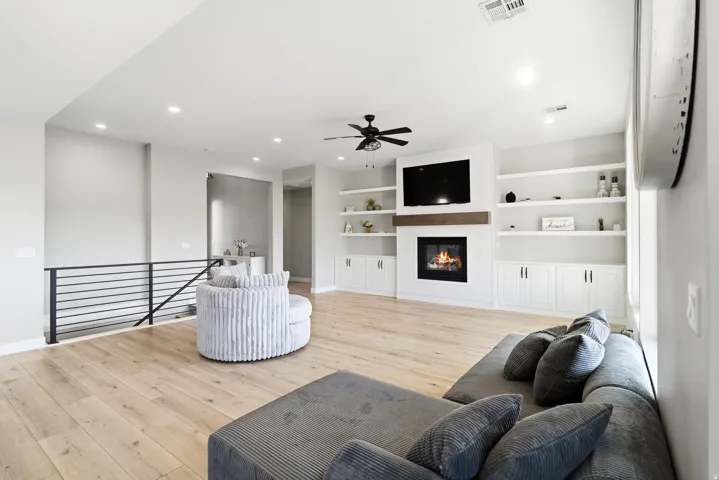 Bright living space featuring wood-finish flooring, a contemporary fireplace with an integrated media center, and custom built-in shelving with lower cabinetry