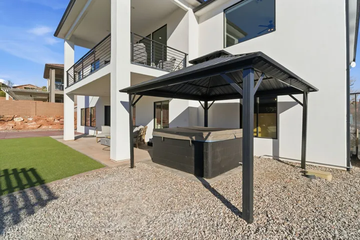 Covered outdoor spa with a metal gazebo structure, adjacent to a manicured artificial turf area