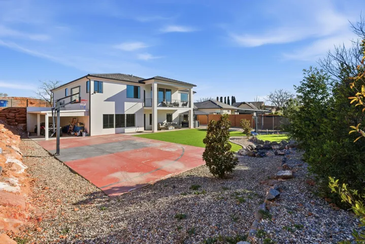 Rear exterior featuring a basketball court, two-story structure with multiple balconies, artificial turf lawn, and a rock-lined dry creek bed