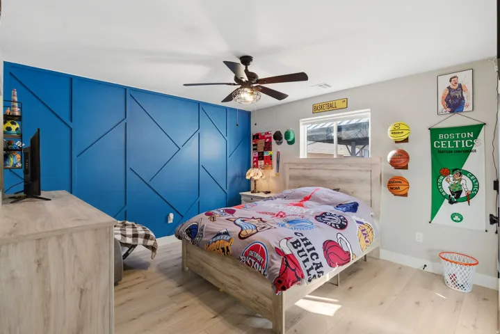 Bedroom featuring a geometric accent wall, wood-finish flooring, and a ceiling fan with integrated lighting