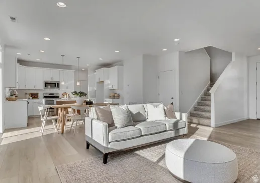 Open-concept living space featuring wood-finish flooring, a contemporary kitchen with white cabinetry and stainless steel appliances, recessed lighting, pendant lighting, and a carpeted staircase. This picture is of another home