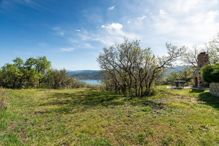 Expansive outdoor space featuring a stone fireplace, mature trees, and natural landscaping