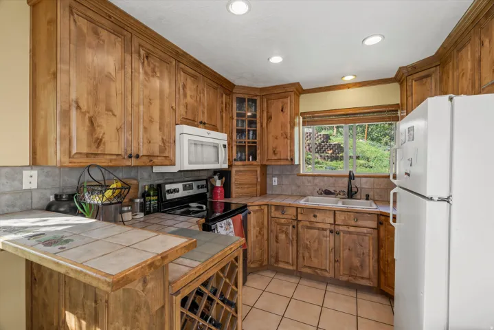 Kitchen featuring wood cabinetry, tile countertops, tile backsplash, and a window overlooking a natural landscape