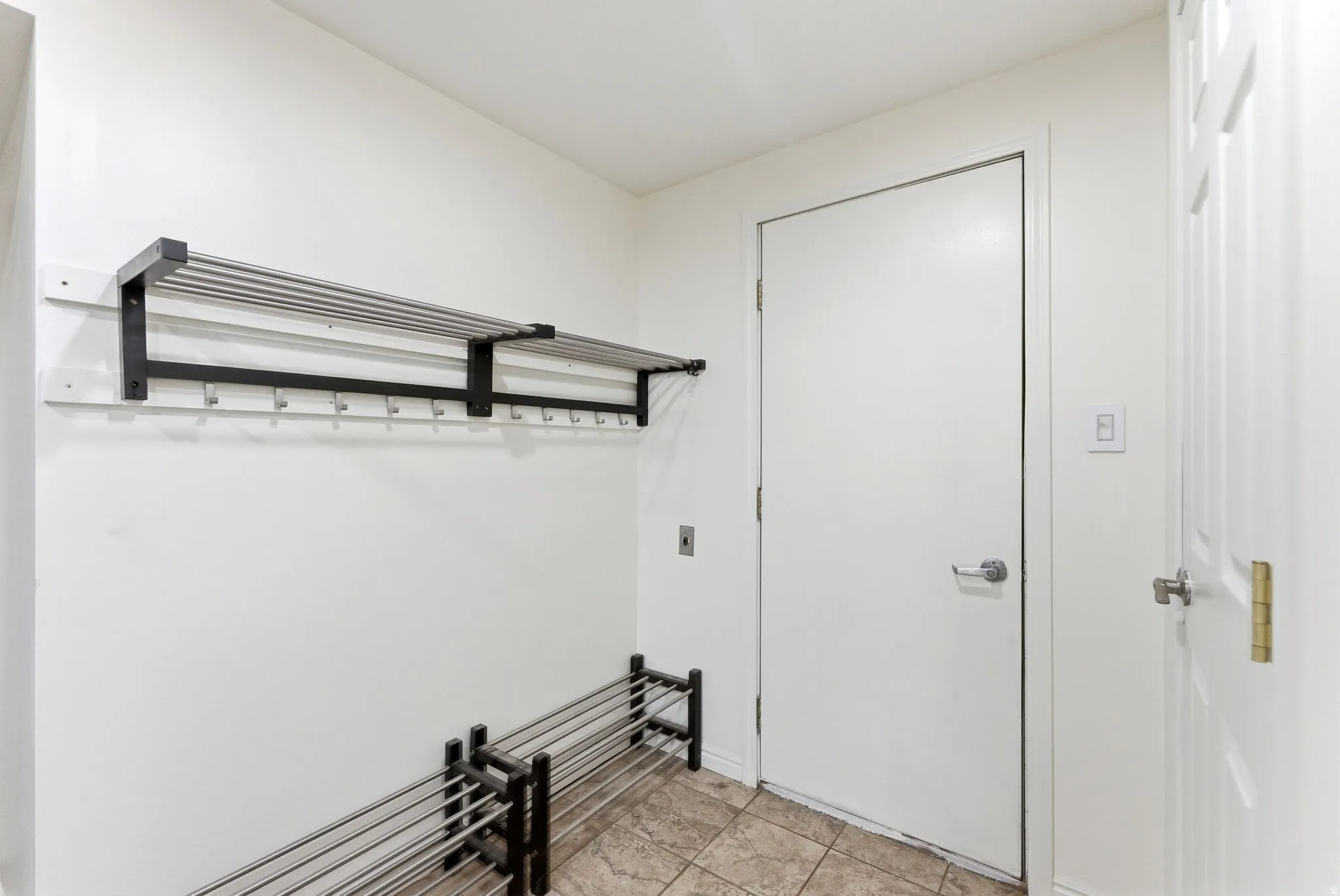 Tiled flooring entry space from garage with built-in wall-mounted coat rack and shoe rack