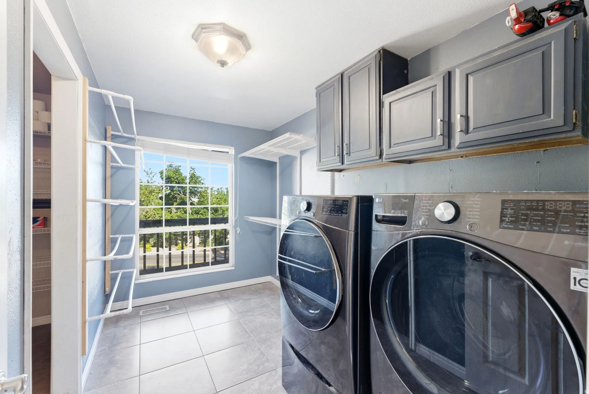Dedicated laundry space featuring ceramic tile flooring, a large window, built-in upper cabinetry, and shelving for organization