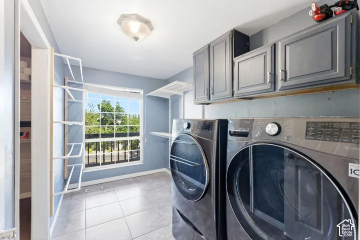 Dedicated laundry space featuring ceramic tile flooring, a large window, built-in upper cabinetry, and shelving for organization
