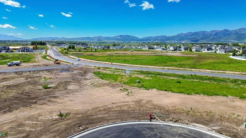 Expansive land parcel featuring a newly paved road, surrounding green fields, and distant mountain ranges