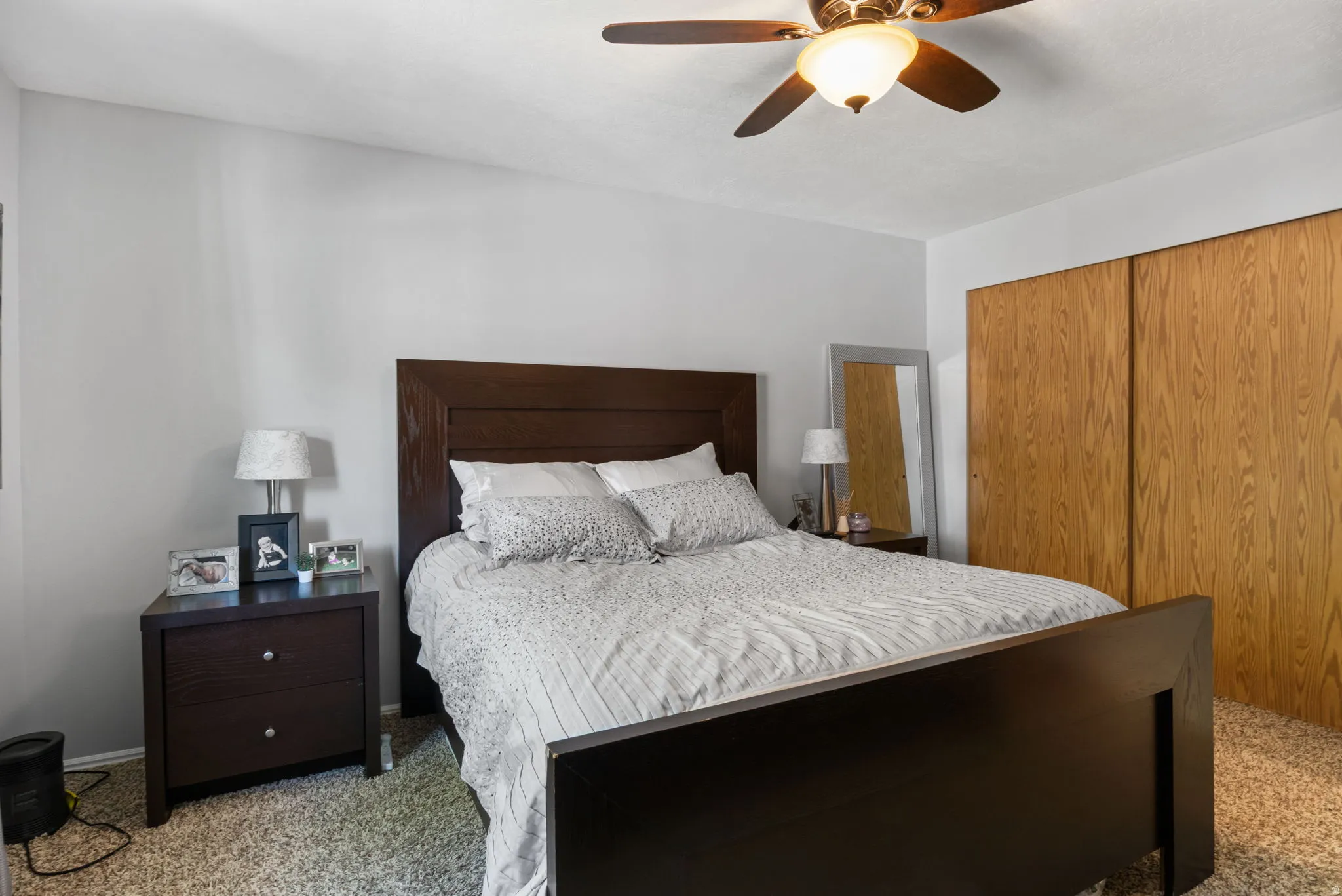 Bedroom featuring light gray walls, wood-finish bi-fold closet doors, a ceiling fan with integrated lighting, and neutral tone carpeting