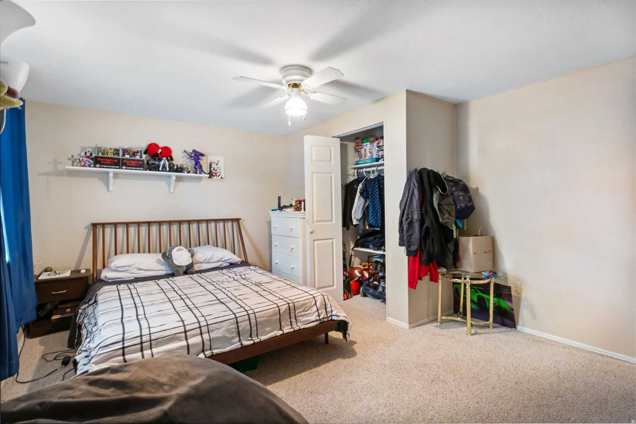 Carpeted room with a ceiling fan, wall shelf, and closet with bifold doors