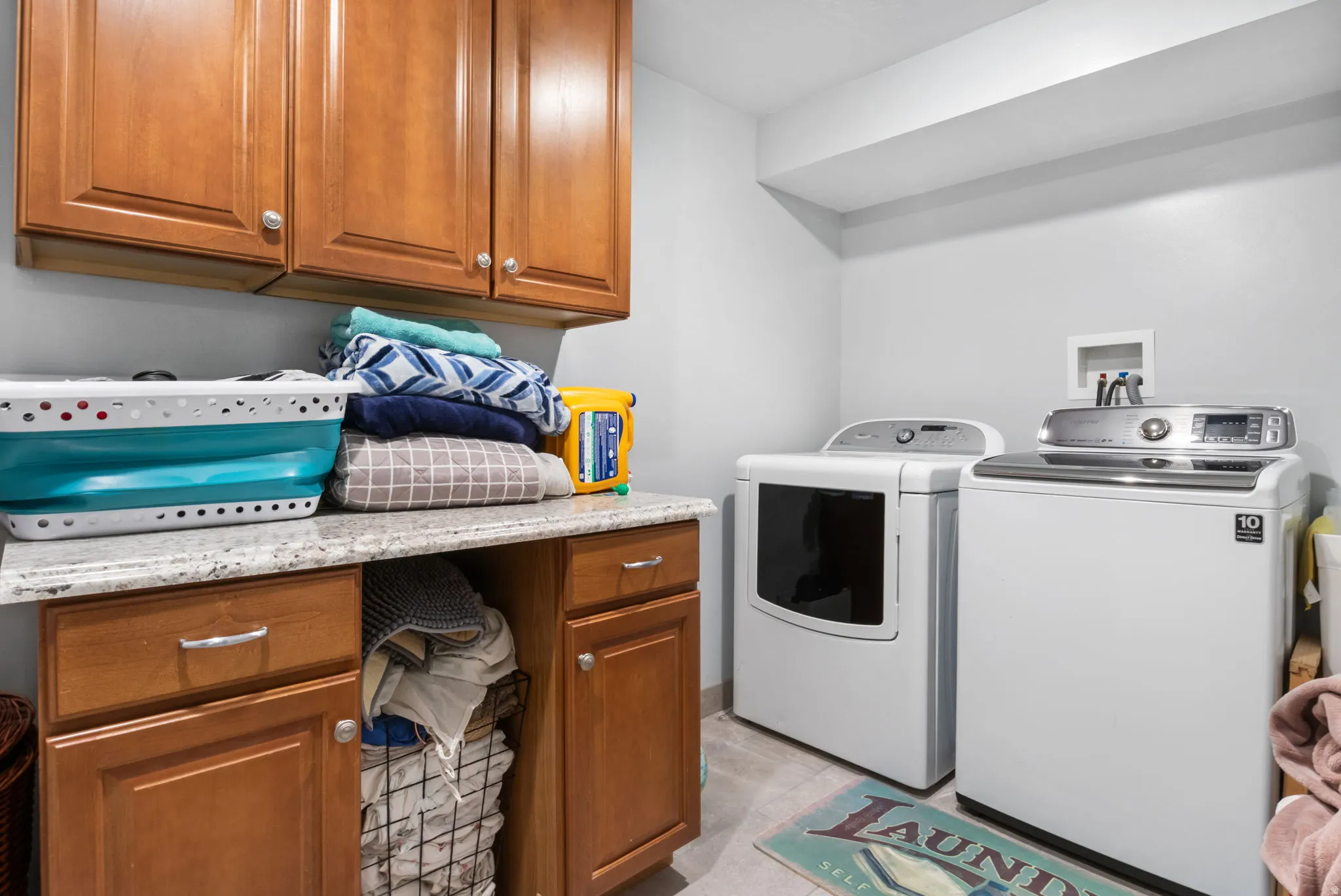 Dedicated laundry room featuring built-in cabinetry, granite-finish countertops, wood-finish flooring, and light gray walls