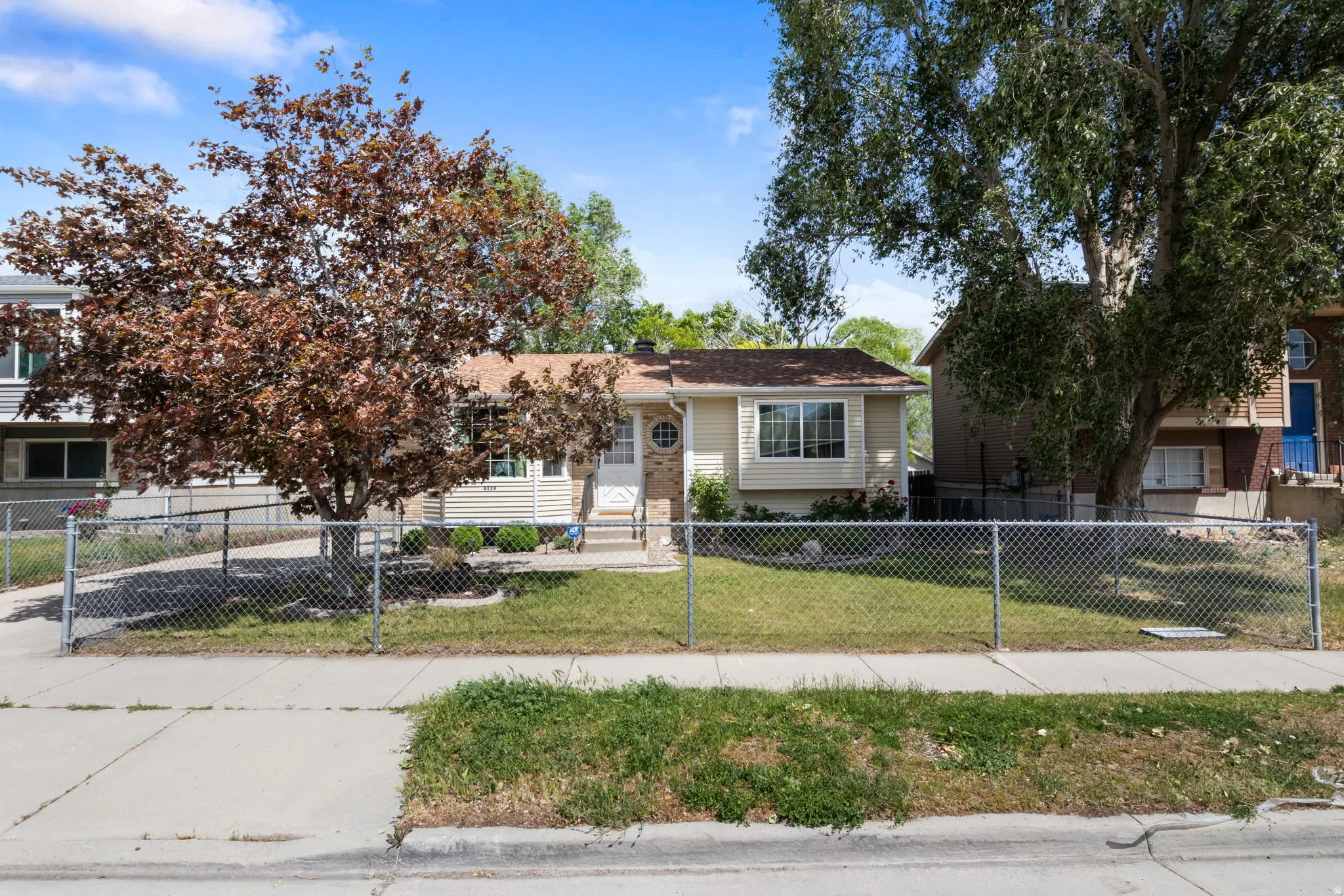 Single-story property featuring light-colored siding, a covered entry, and a chain-link fence enclosing the front yard