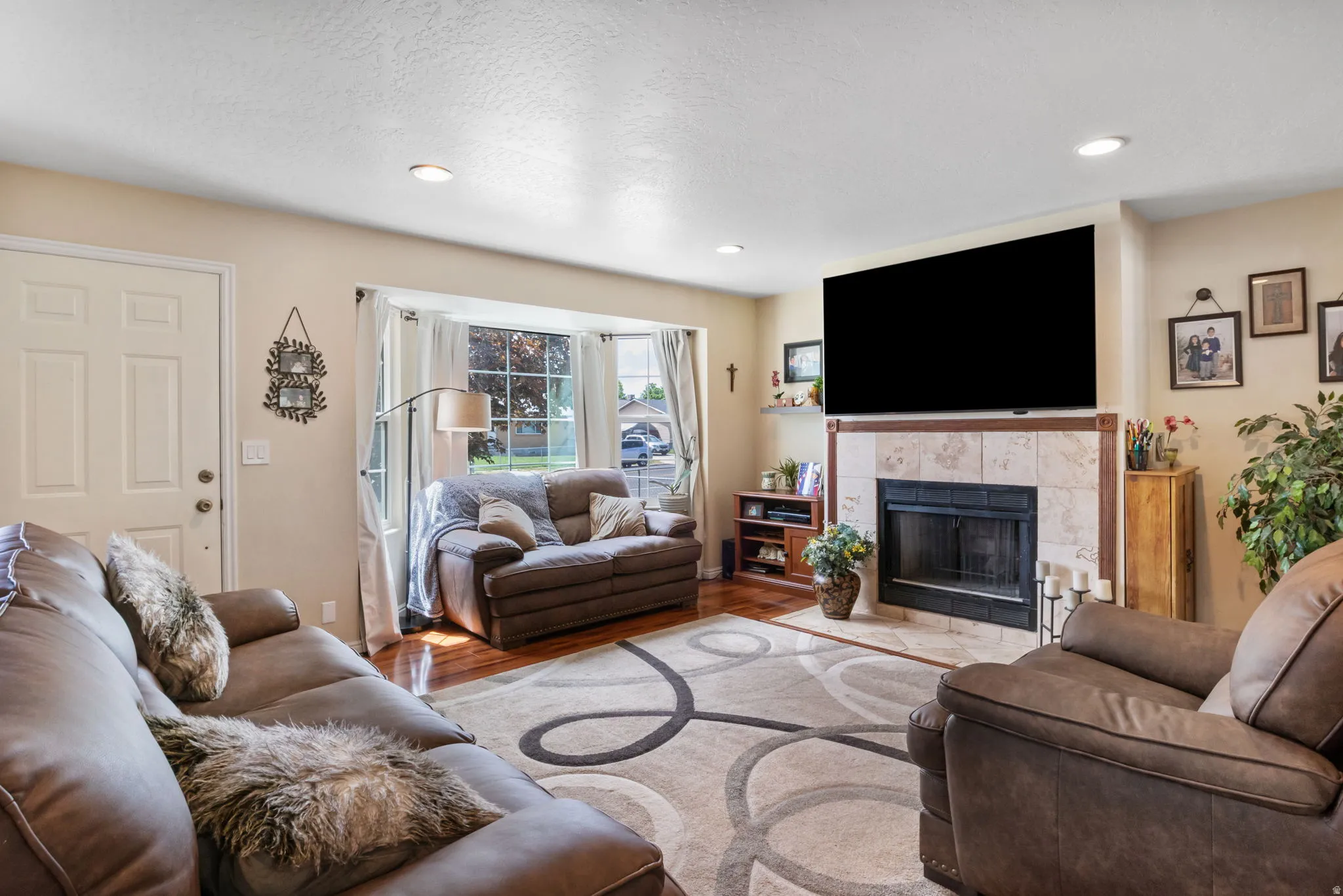 Living area featuring a bay window with window treatments, recessed lighting, wood-finish flooring, and a fireplace with a tile surround and hearth