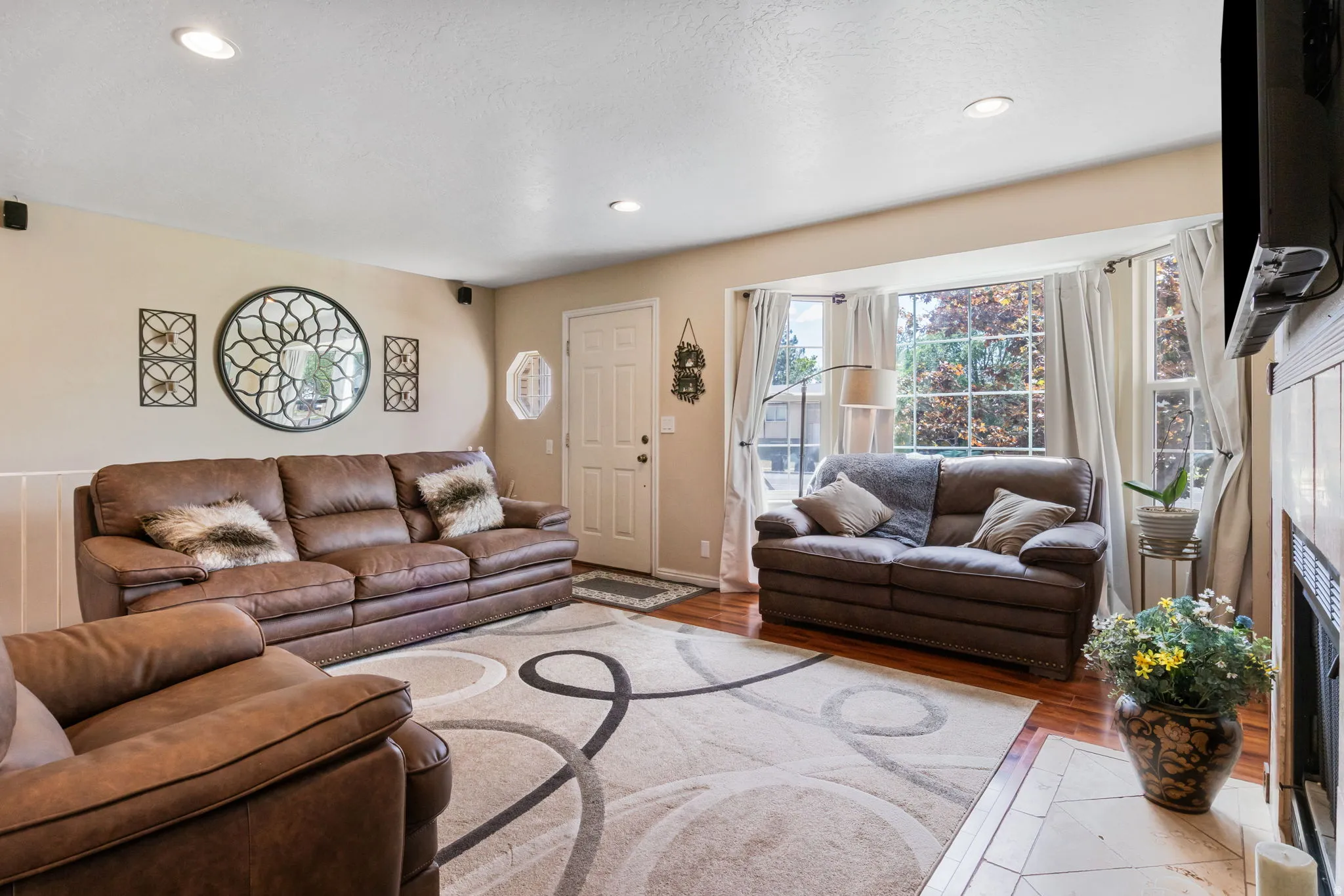 Living area featuring polished wood flooring, a front entry door, recessed ceiling lighting, a bay window with window treatments, and a fireplace with a wood mantel