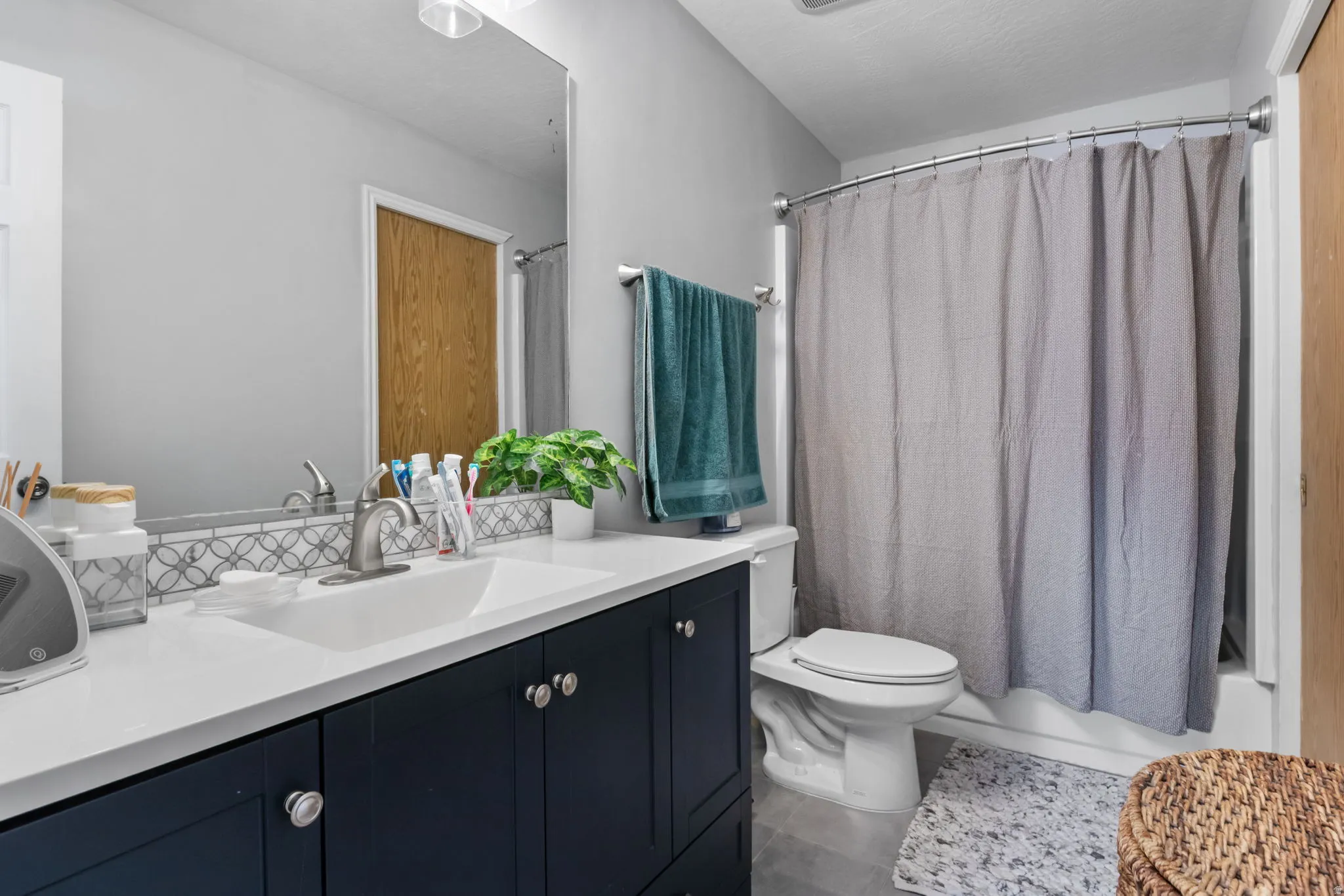 Bathroom featuring a dark blue vanity with a white countertop and integrated sink, a tiled backsplash with a decorative pattern, a toilet, and a shower/tub combination with a curved shower rod