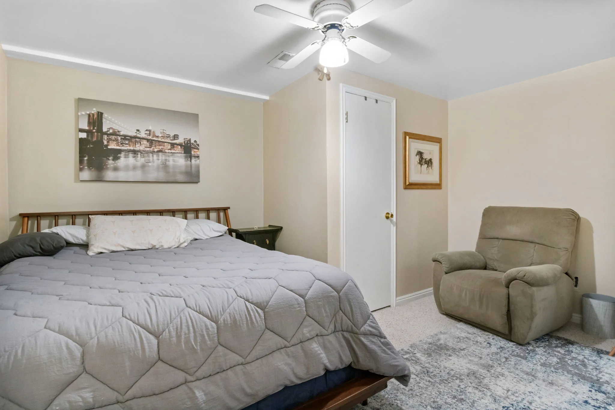 Carpeted bedroom featuring a ceiling fan with integrated lighting, neutral wall tones, and a solid white door with a brass-finish doorknob