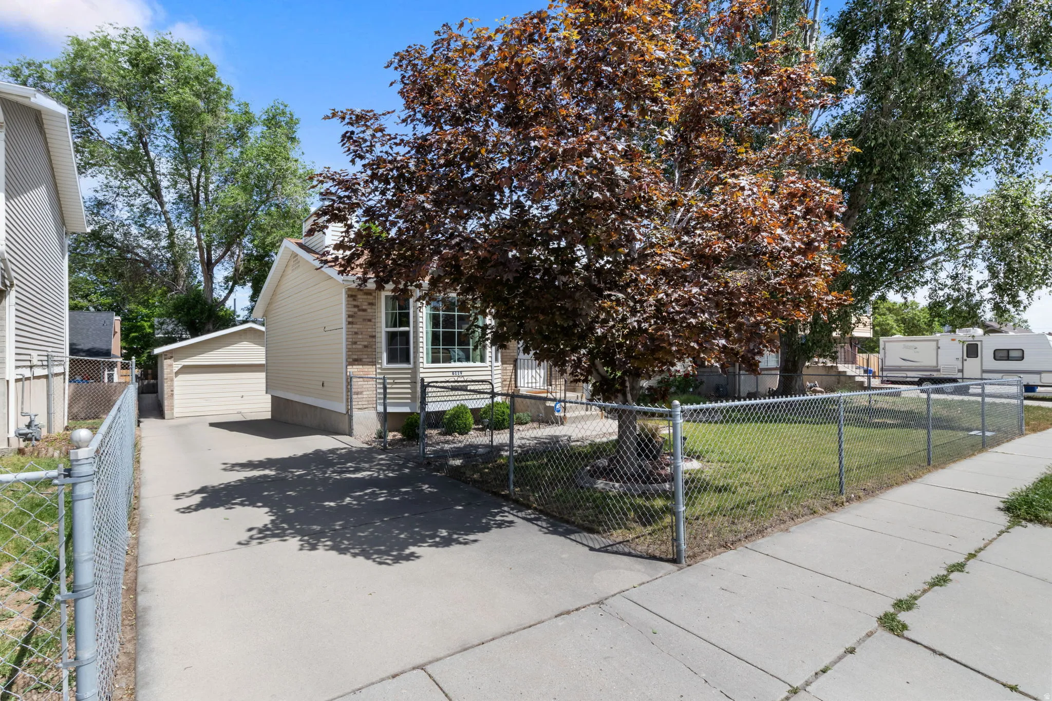 Front exterior featuring a chain-link fence, mature trees, a paved driveway, and a detached garage