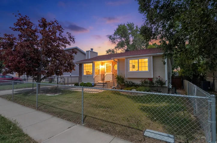 Exterior featuring beige horizontal siding, a chain-link fence, mature trees, a front lawn, and a paved sidewalk