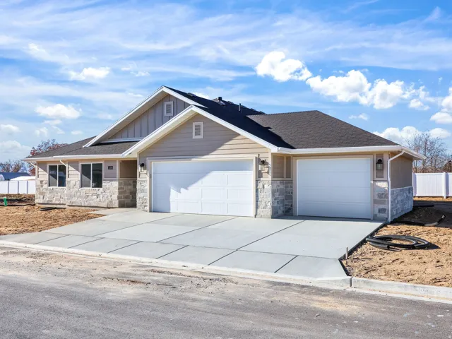Contemporary-style residence featuring a two-car garage with white doors, light-toned horizontal siding, and stone veneer accents
