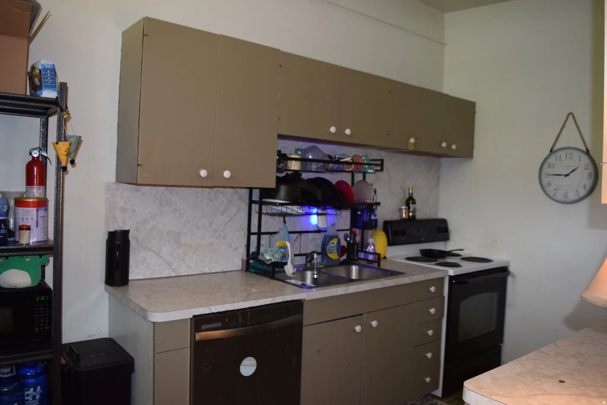 Kitchen featuring a double basin stainless steel sink, built-in dishwasher, white electric range, and light-colored countertops with a matching backsplash