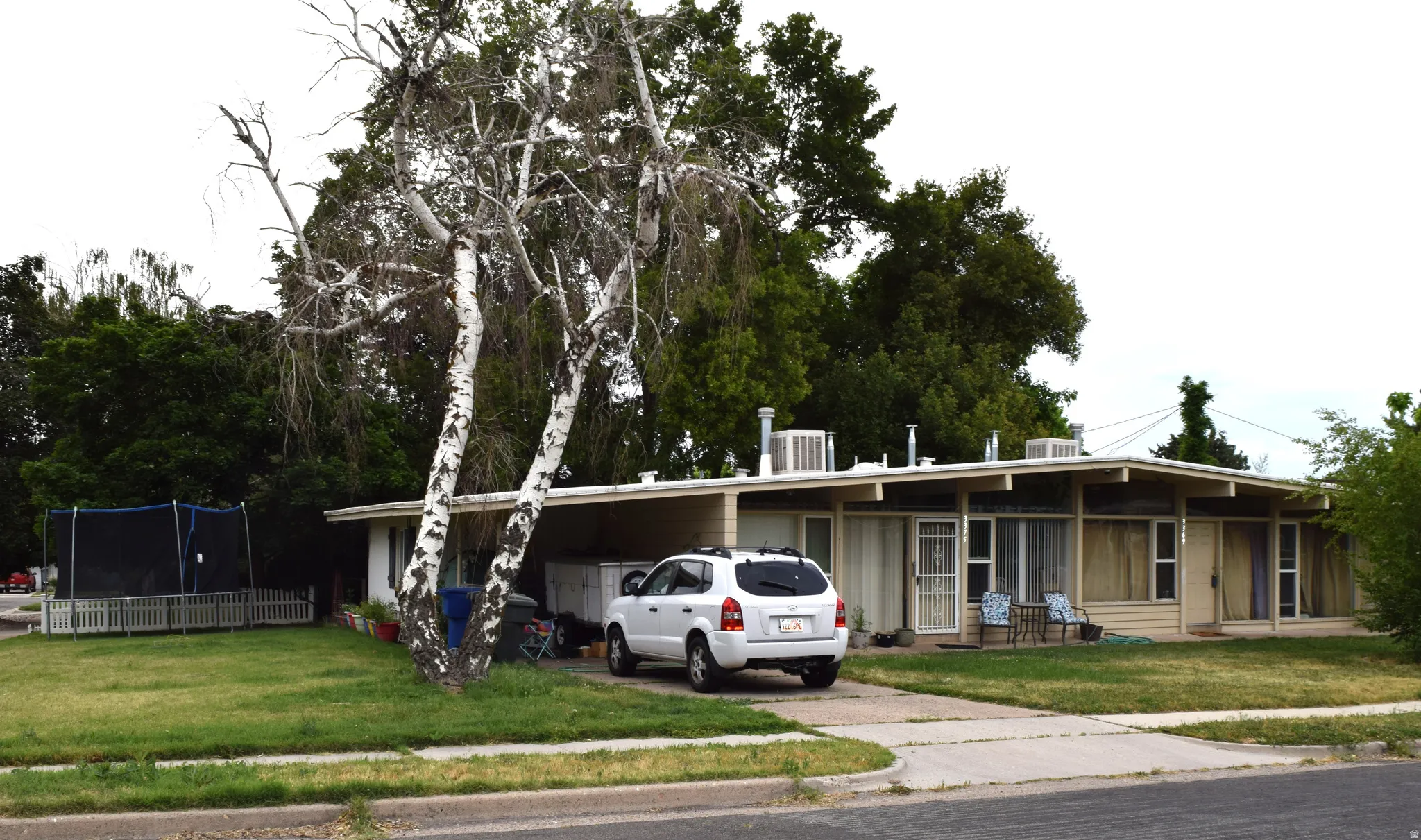 Single-story residence featuring a carport, front lawn, and mature trees