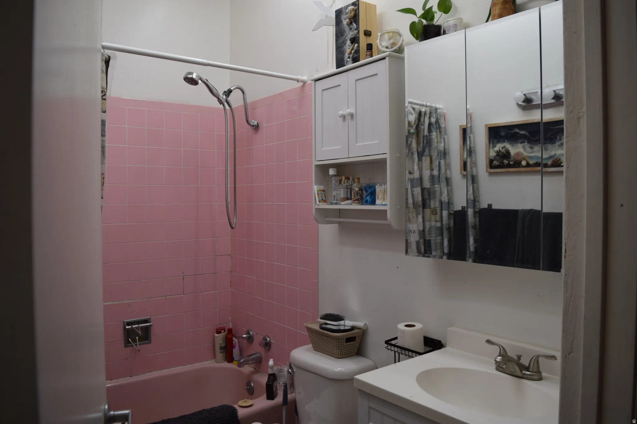 Bathroom featuring pink tiled shower surround, coordinated pink bathtub, white vanity with integrated sink, chrome faucet, and mirrored medicine cabinet