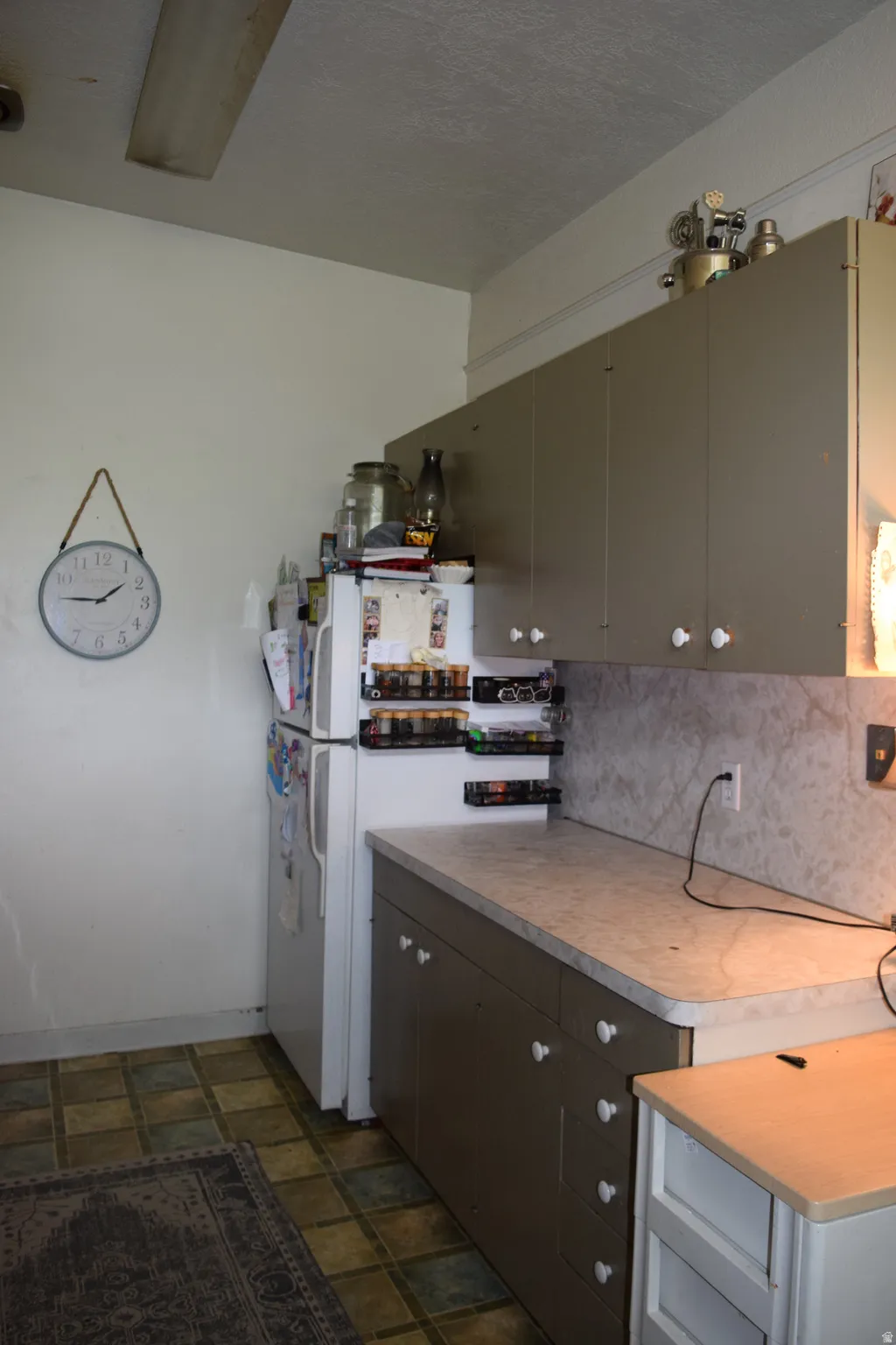 Kitchen featuring upper and lower cabinetry with white knobs, a white refrigerator, a light-colored countertop, and a tiled floor