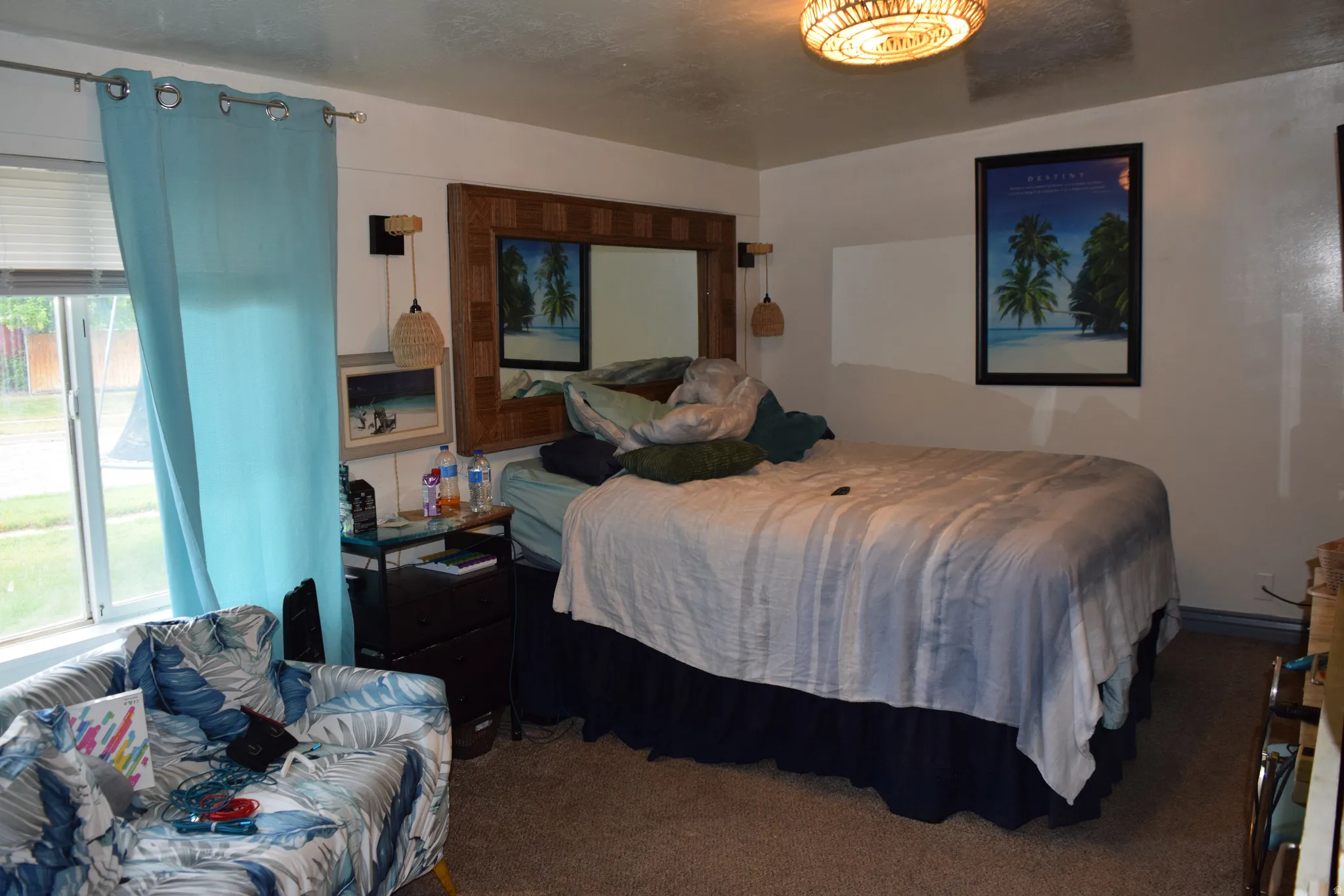 Carpeted bedroom featuring a window with blinds, a wall-mounted light fixture, and a decorative ceiling light