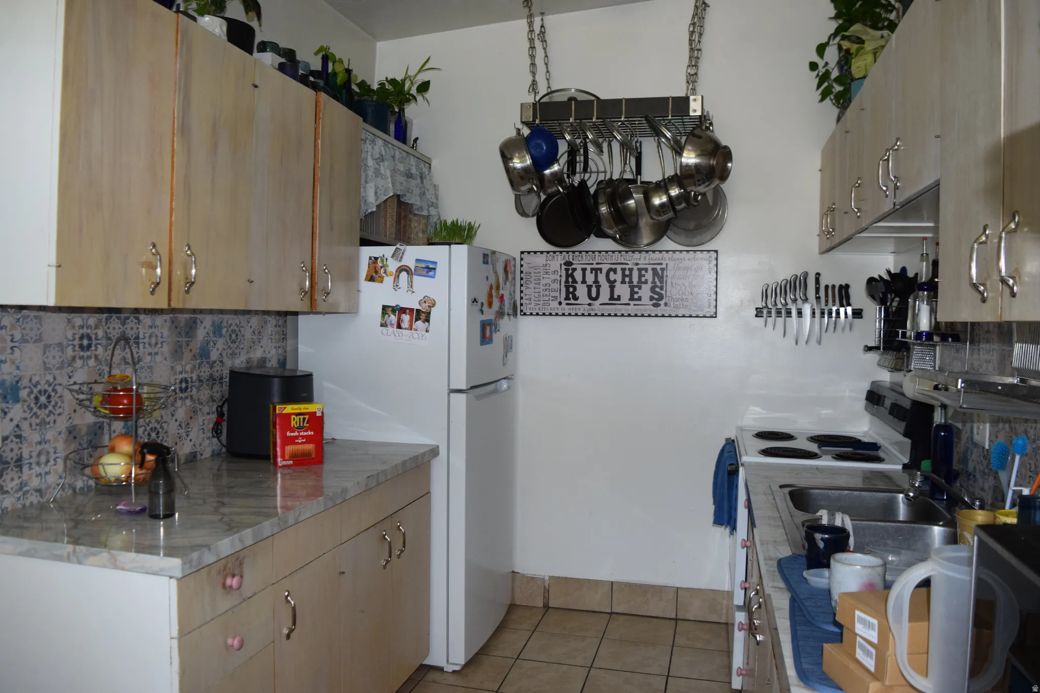 Galley kitchen featuring wood-finish cabinetry with silver hardware, patterned tile backsplash, and light-colored countertops