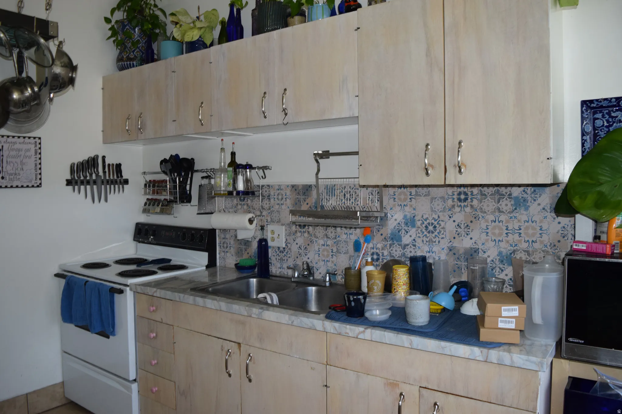 Kitchen featuring a double basin sink, light-toned upper and lower cabinetry with varied hardware, and a patterned tile backsplash