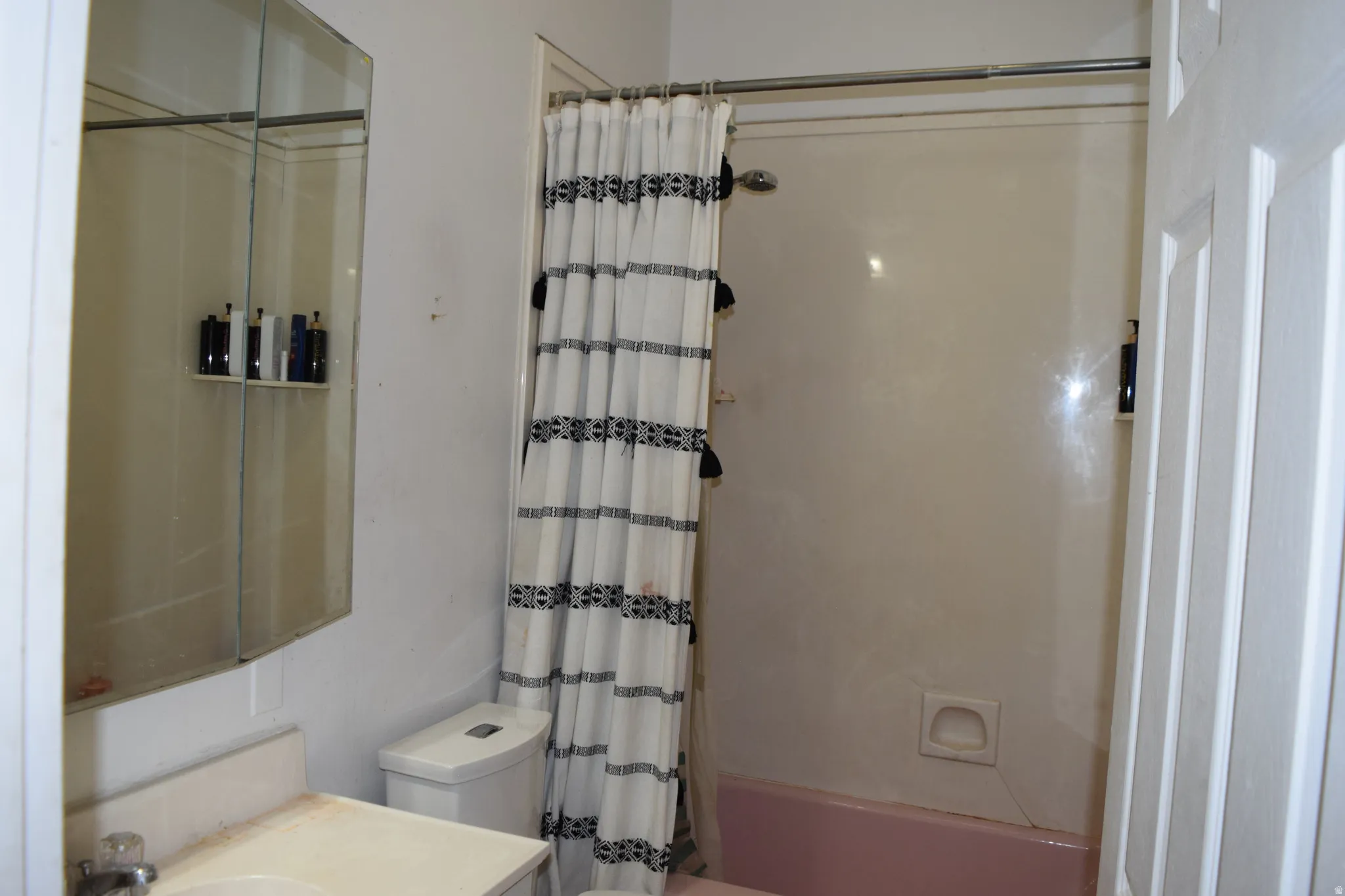 Bathroom featuring a white vanity with an integrated sink, a mirrored medicine cabinet, a toilet, and a shower/tub combination with a shower curtain