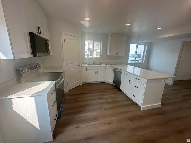 Modern kitchen featuring wood-finish flooring, white cabinetry with black hardware, a center island, recessed lighting, and stainless steel appliances including a range and microwave