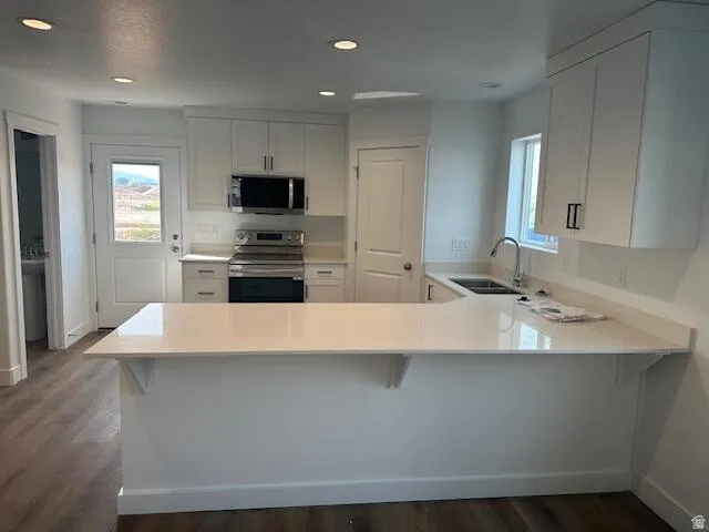 Contemporary kitchen featuring an eat-at peninsula with light-toned countertops, white cabinetry, stainless steel appliances, and recessed lighting