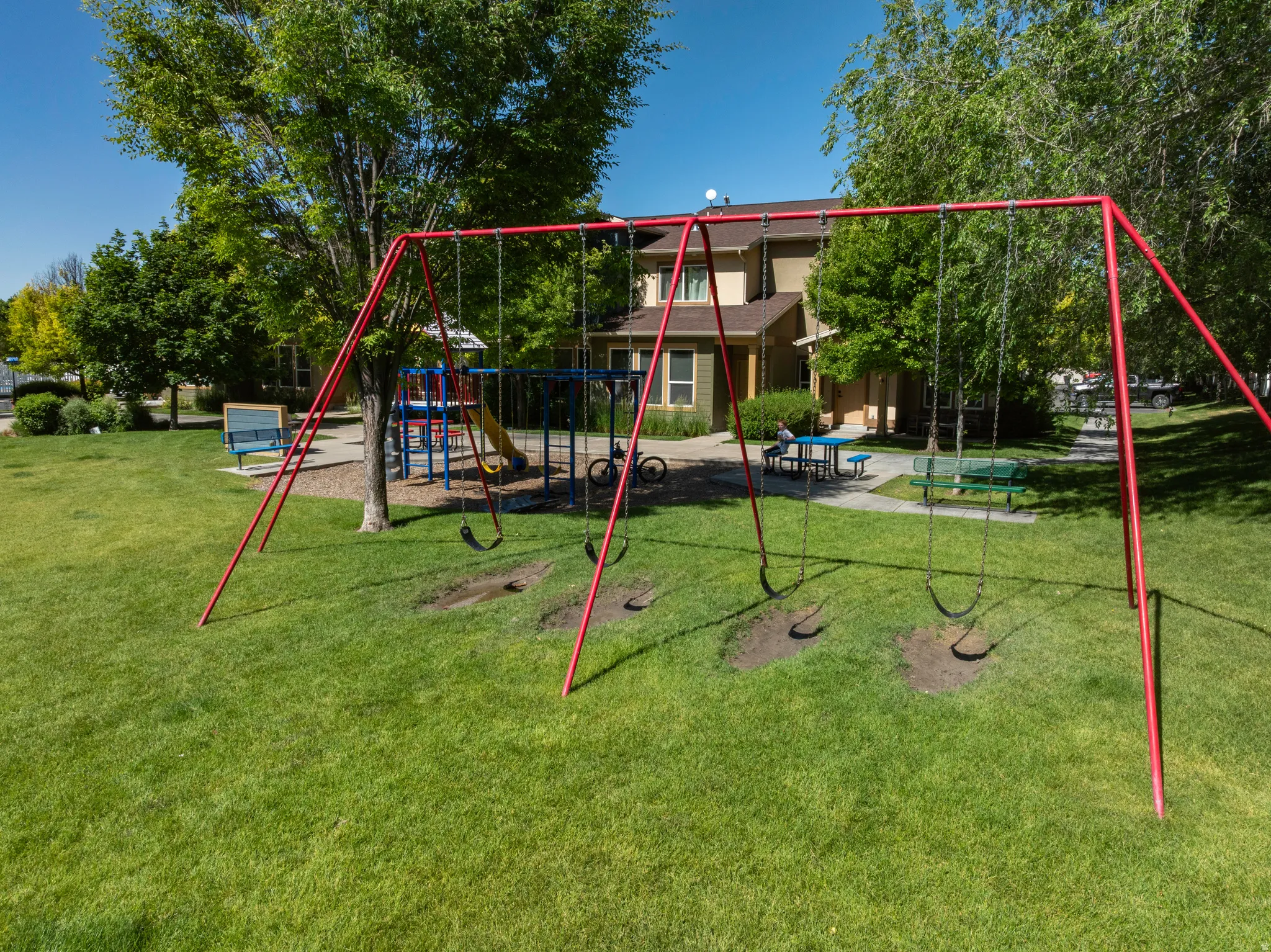Expansive green space featuring a red swing set, a separate play structure with a slide, and mature trees