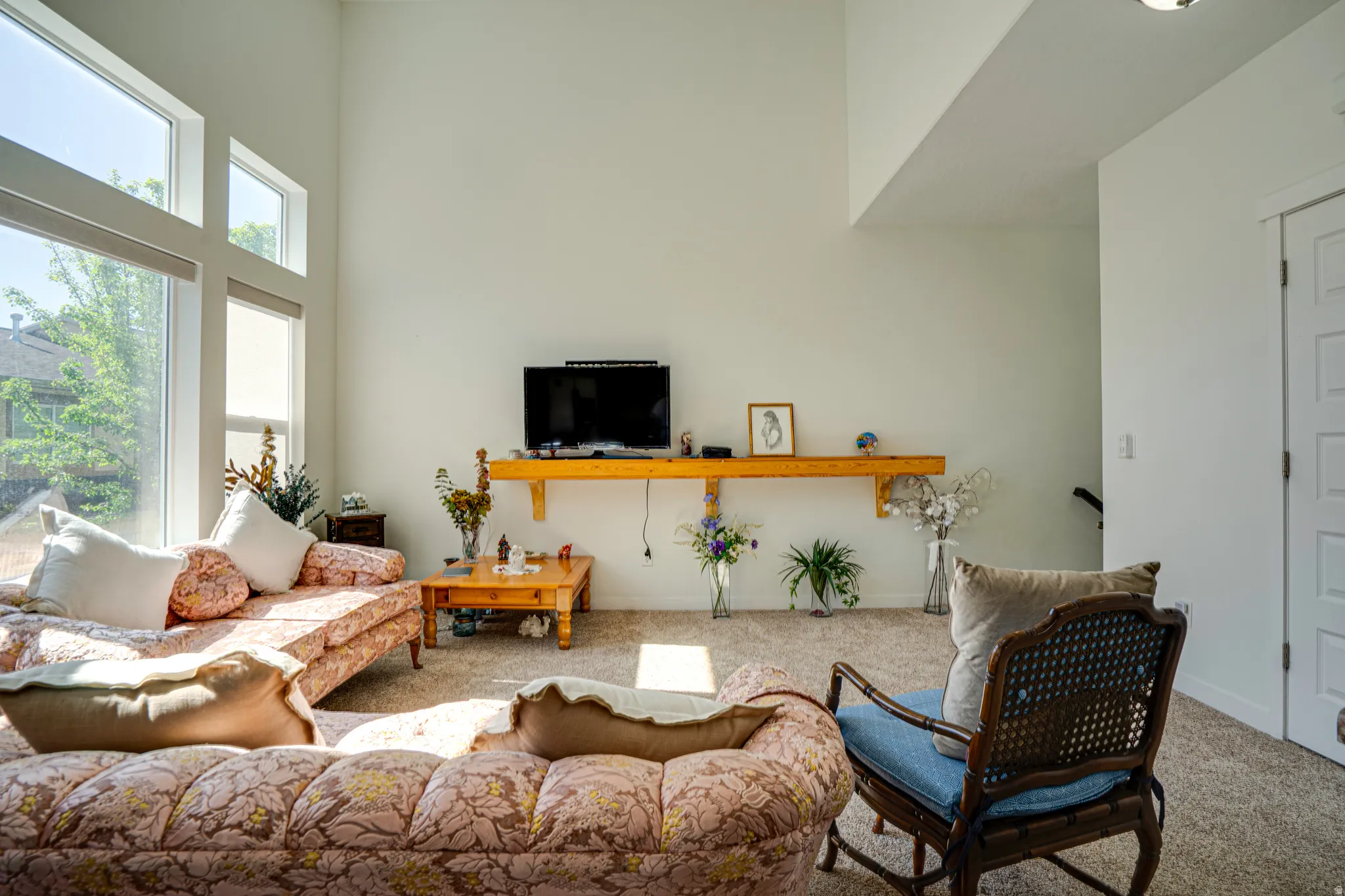 Living area featuring vaulted ceilings, large picture windows, wood-finish shelving, and neutral wall tones
