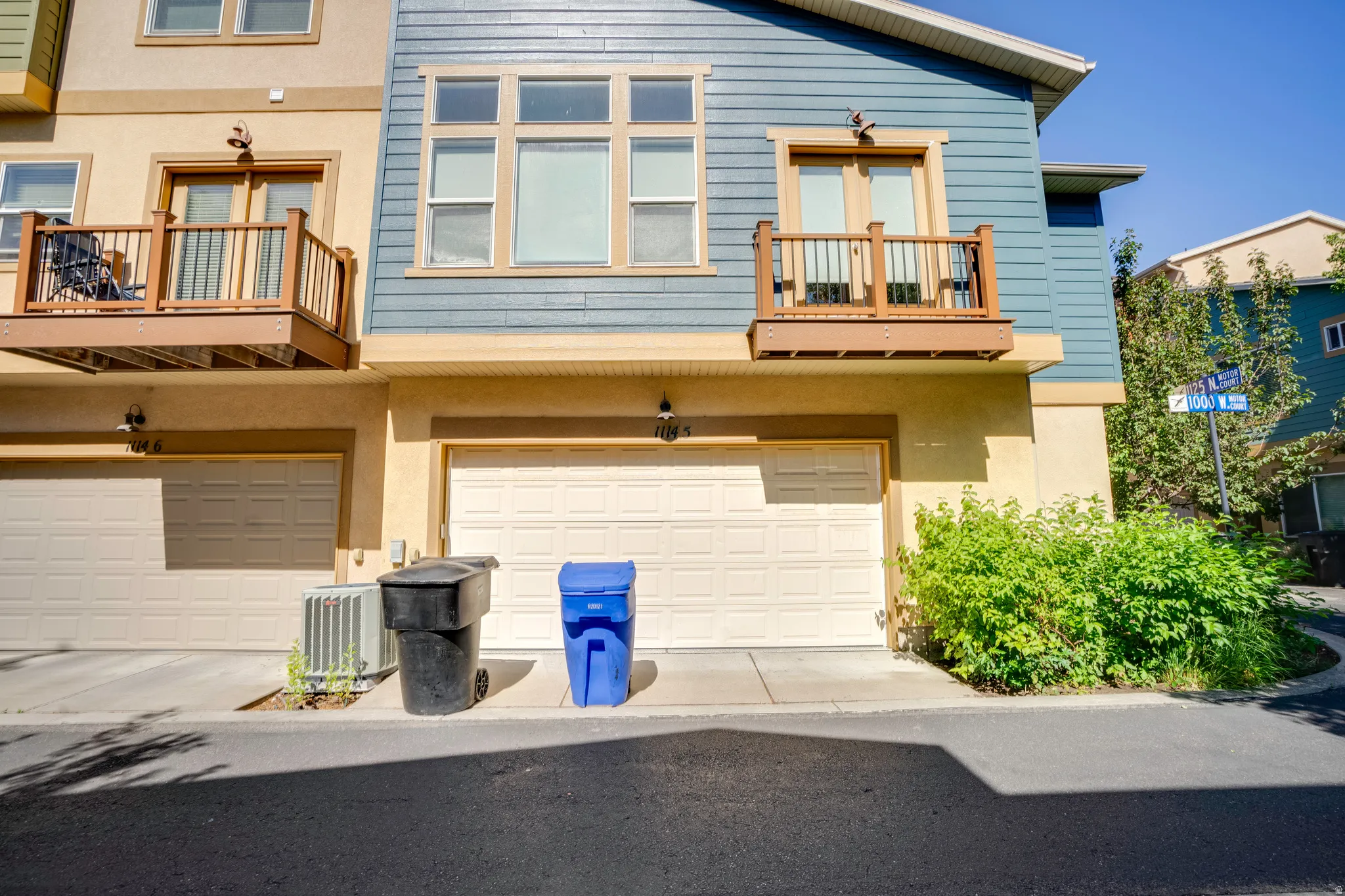 Townhome exterior featuring a two-car garage, upper-level balcony with wood railing, and blue horizontal siding