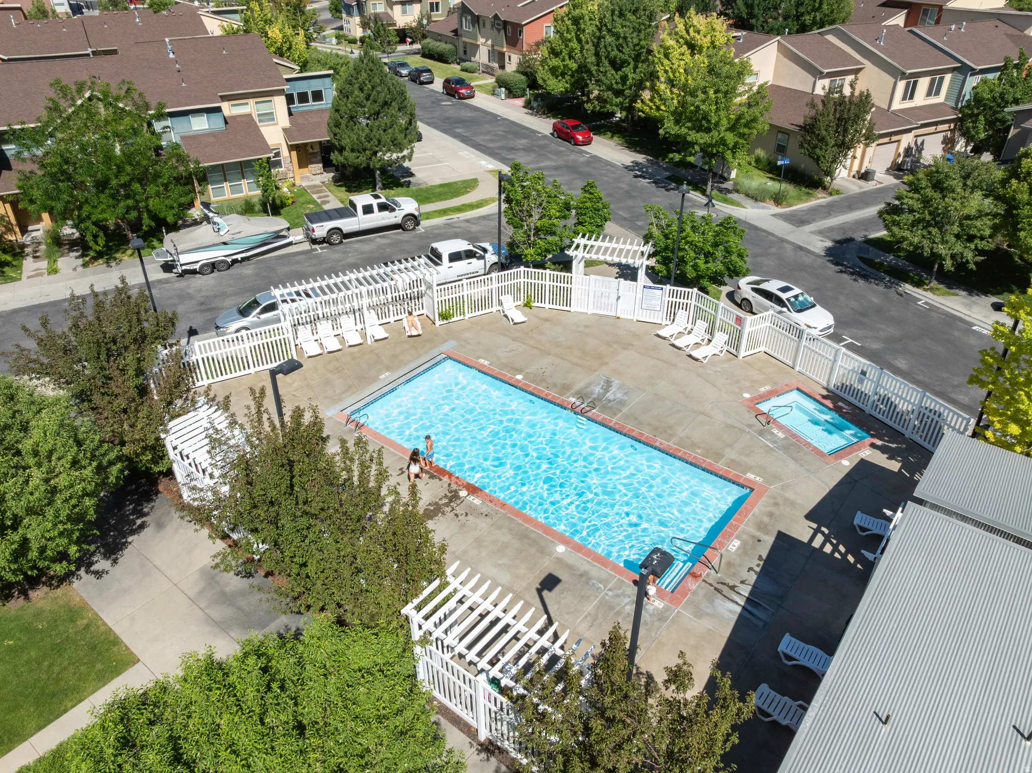Community swimming pool and spa with surrounding white picket fencing, concrete decking, and lounge seating