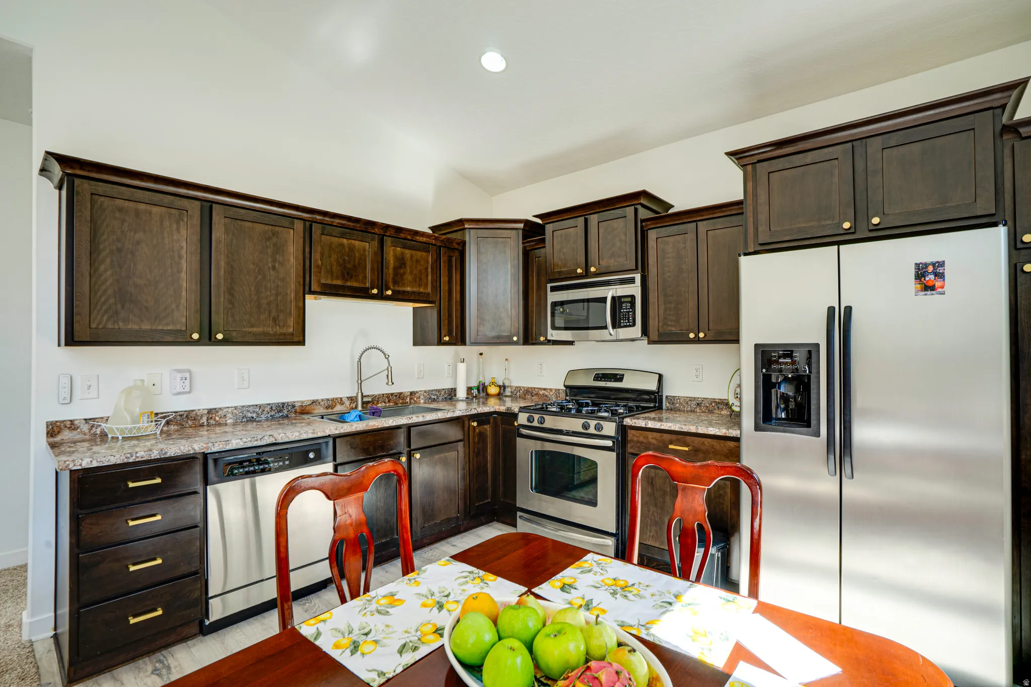 Kitchen featuring dark wood-finish cabinetry, stainless steel appliances, speckled countertops, and a double basin sink with a gooseneck faucet