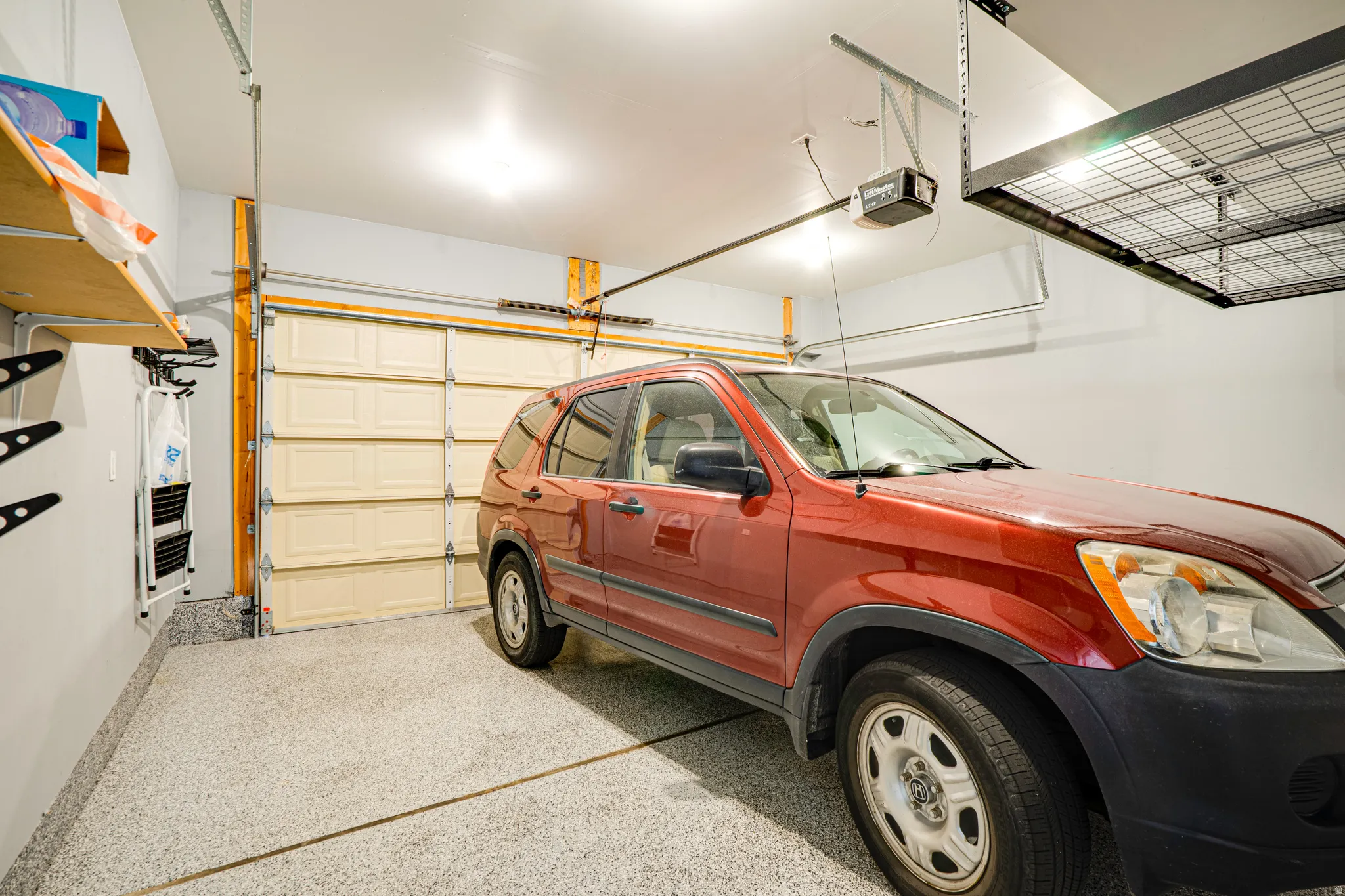 Attached garage featuring an epoxy-coated floor, overhead storage racks, an automatic garage door opener, and integrated wall shelving