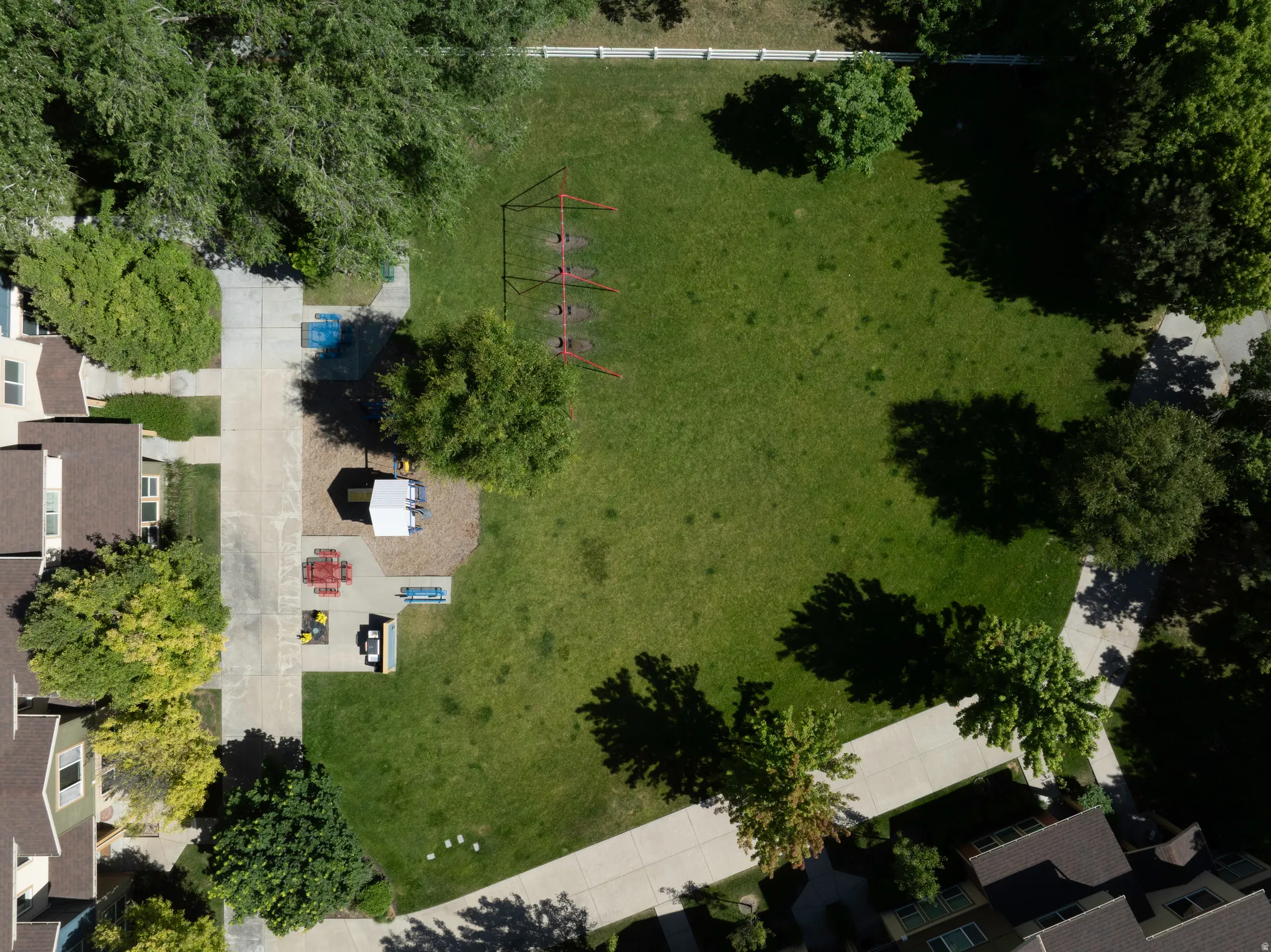 Manicured green space featuring a large lawn area, mature trees, concrete pathways, and recreational equipment
