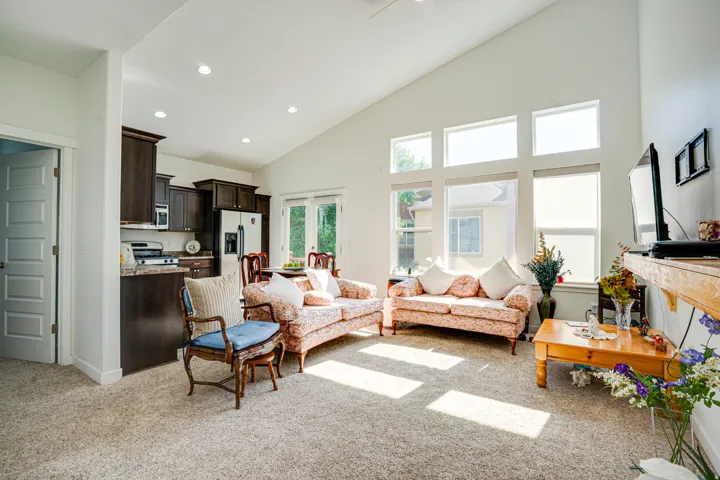 Vaulted ceilings enhance this open-concept living area, featuring a wall of windows, recessed lighting, and soft carpeting