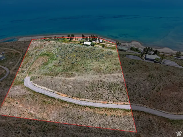Expansive land parcel featuring a curved asphalt road, natural vegetation, and direct water frontage