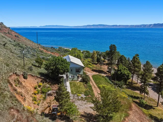Lakefront property featuring a sloped, natural landscape and mature trees