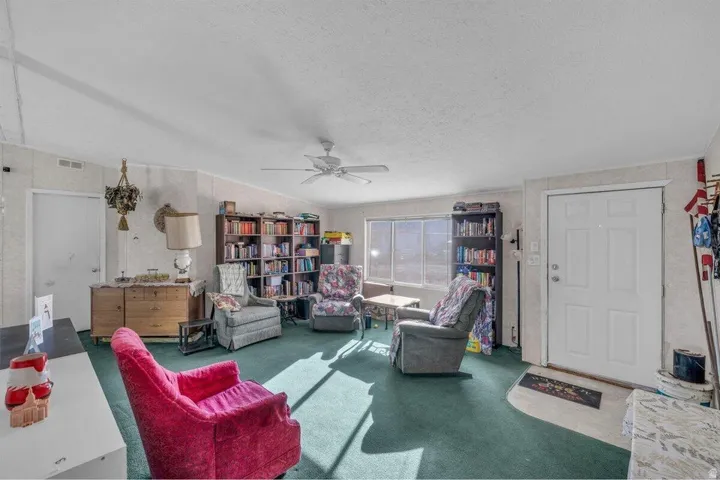 Spacious living area featuring a ceiling fan, broad windows, and a front entry door with paneling