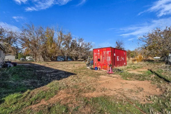 Expansive lot featuring a large red storage container, mature perimeter trees, and a clear blue sky