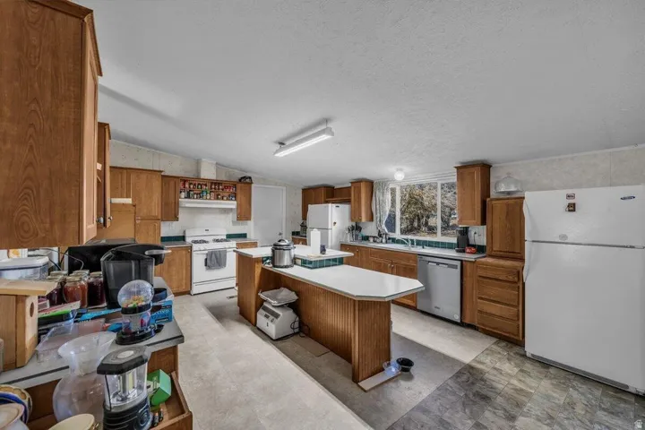 Spacious kitchen featuring warm wood cabinetry, a central island with white countertops, and dual white refrigerators