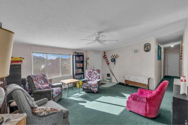 Living area featuring wall-to-wall carpeting, textured wall finishes, and a ceiling fan with integrated lighting