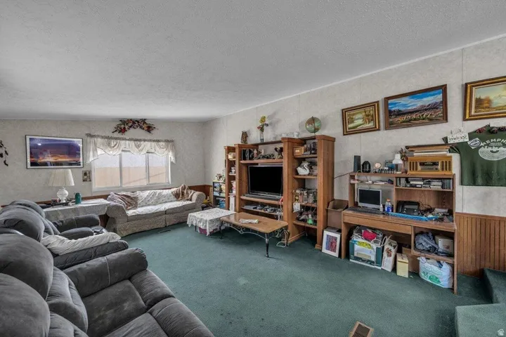 Spacious interior room featuring light-colored walls, green carpeting, and a large window with white blinds