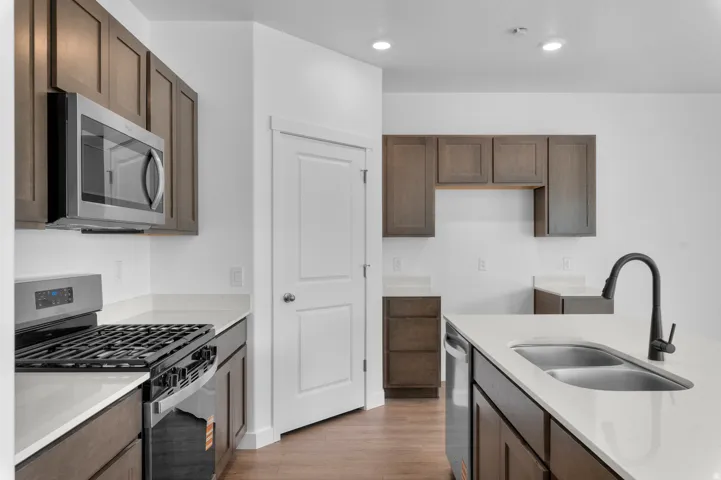 Modern kitchen featuring wood-finish cabinetry, light-toned countertops, and stainless steel appliances including a microwave and gas range