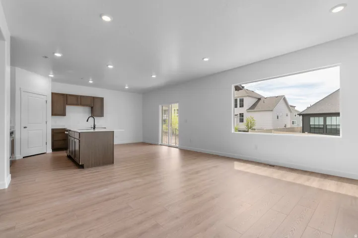 Open-concept living area featuring light wood-finish flooring, recessed lighting, and a prominent kitchen island with an undermount sink