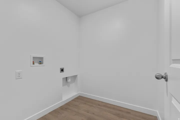 Dedicated laundry area featuring wood-finish flooring, white walls, and a white paneled door with a brushed nickel knob